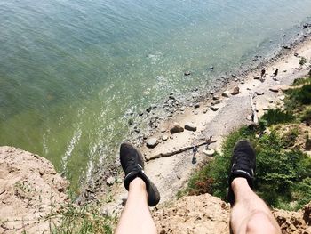 Low section of man sitting on cliff over sea during sunny day