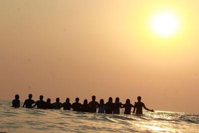 People on sea against sky during sunset