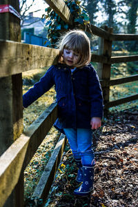 Girl standing by wooden fence on field