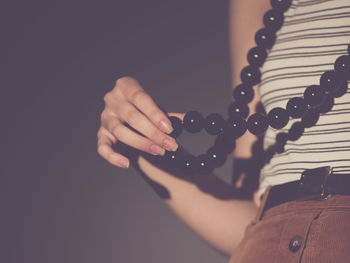 Midsection of woman wearing necklace against gray background