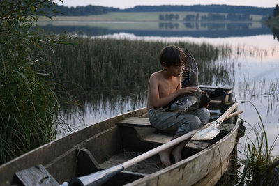 Boy holding bird while sitting in boat on lake