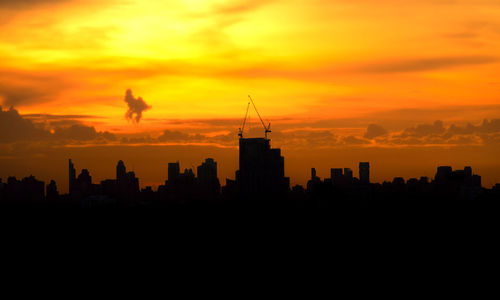 Silhouette of city against cloudy sky during sunset