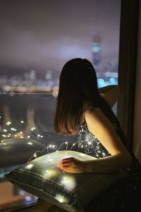 Woman holding illuminated string light looking through window at home
