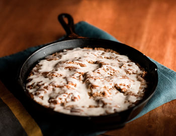 Glazed cinnamon rolls inside cast iron skillet on wood table