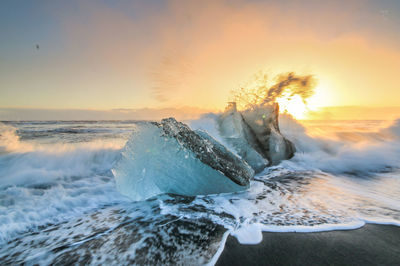 Waves splashing on sea against sky during sunset