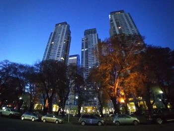 Cars on illuminated modern buildings in city against sky