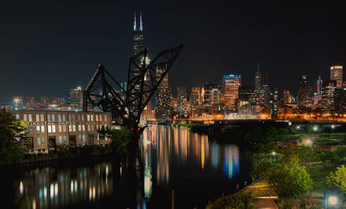Illuminated buildings by river against sky at night