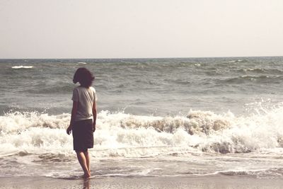 Rear view of boy standing on beach against clear sky