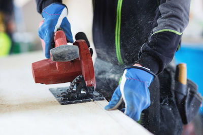 Midsection of manual worker using jigsaw on wooden planks at site