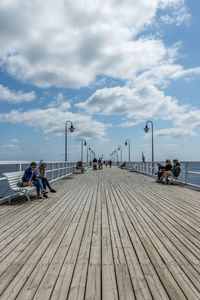 People on pier by sea against sky