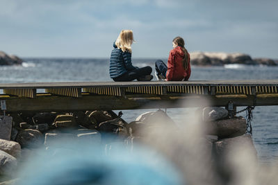 People sitting on pier over sea against sky