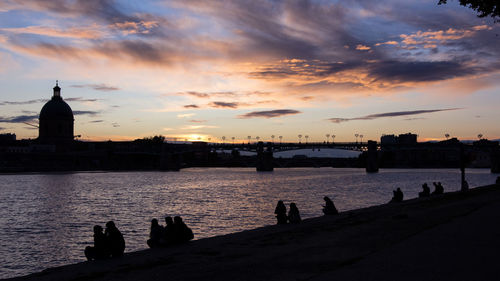 Silhouette people by sea against sky during sunset