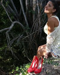 Woman with red high heels sitting against tree