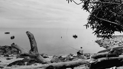 Man fishing in sea against sky