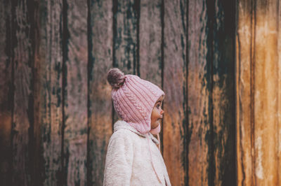 Close-up of toddler wearing knit hat standing by wooden wall
