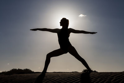 Silhouette woman exercising against sky during sunset