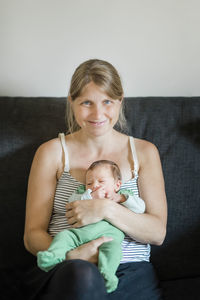 Portrait of woman holding toddler son while sitting on sofa