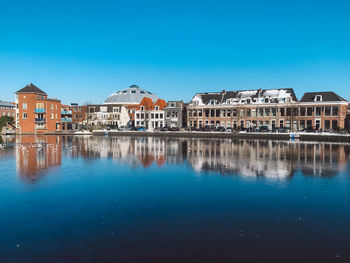 Buildings by lake against blue sky