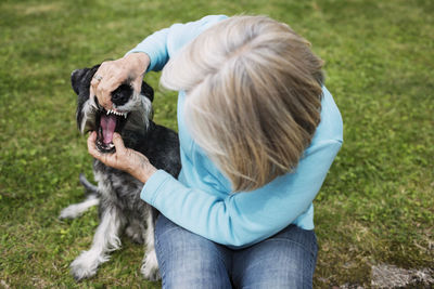 Senior woman examining dog's mouth while sitting at yard