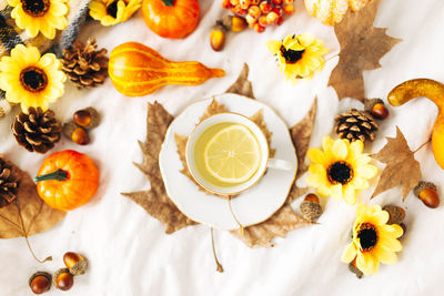 Top view of a cup of lemon tea surrounded by sunflowers, pumpkins, leaves, acorns, pine cones 
