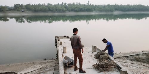 Rear view of men sitting by lake