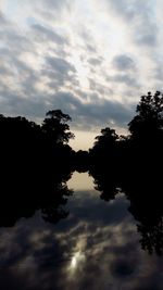 Silhouette trees by lake against sky during sunset