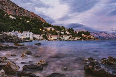 View of houses in front of sea against cloudy sky