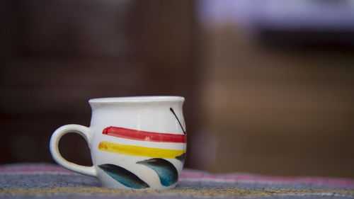 White porcelain tea cup with red and yellow line decoration and a sofa, on home background.
