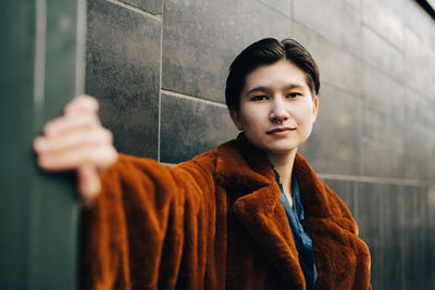 Portrait of young woman standing against wall