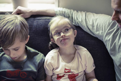 Girl with down syndrome looking at father by brother on sofa