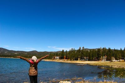 Woman standing on lakeshore against clear blue sky