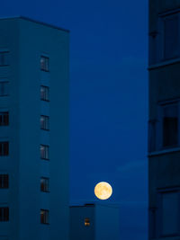 Low angle view of skyscraper buildings against sky at night with full moon