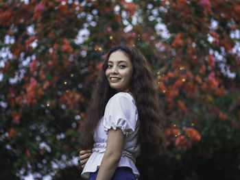 Portrait of smiling young woman standing against trees during autumn