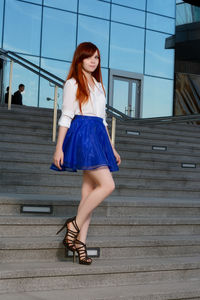 Portrait of beautiful redhead woman standing on staircase against building