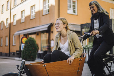 Happy mature businesswoman riding cargo bicycle with female colleague in city