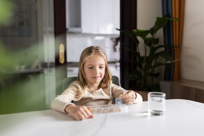 Girl with medicine sitting by table at home