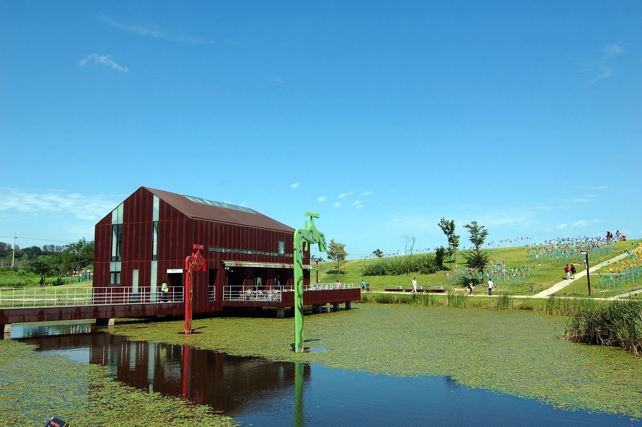 water, built structure, architecture, building exterior, blue, sky, grass, tree, river, lake, house, railing, tranquility, reflection, nature, plant, day, tranquil scene, outdoors, no people