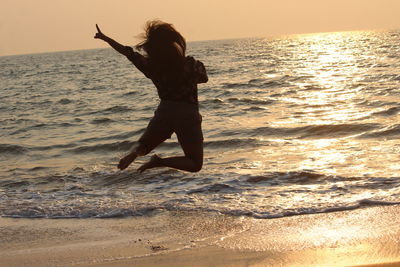 Silhouette woman jumping at beach against sky during sunset