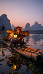 Portrait of man wearing hat crouching on raft against mountain and sky