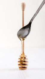 Close-up of honey pouring from spoon on dipper against white background