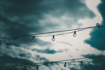 Low angle view of water drops on cable against sky