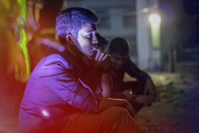 Side view of thoughtful man looking away while sitting outdoors at night