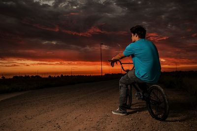 Man sitting on bicycle over land against cloudy sky