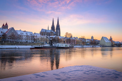 Regensburg cathedral and snow covered houses by danube river during sunset