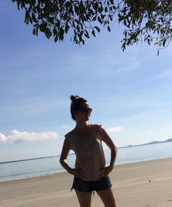 Young woman standing at beach against sky