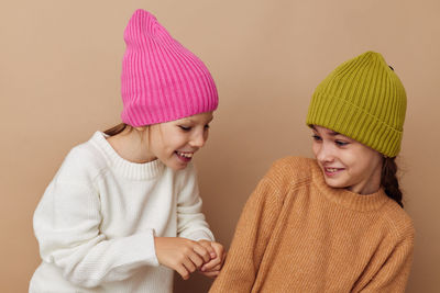 Happy friends wearing knit hat standing against beige background