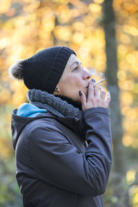 Side view of mature woman smoking while standing at park during winter