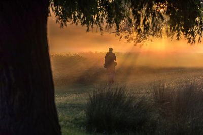 Silhouette man on field against sky during sunset