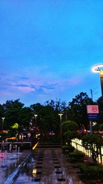 Illuminated street lights by trees against blue sky