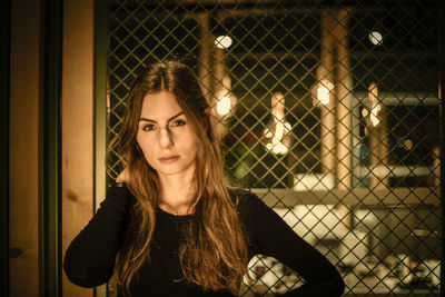 Portrait of smiling young woman standing against chainlink fence